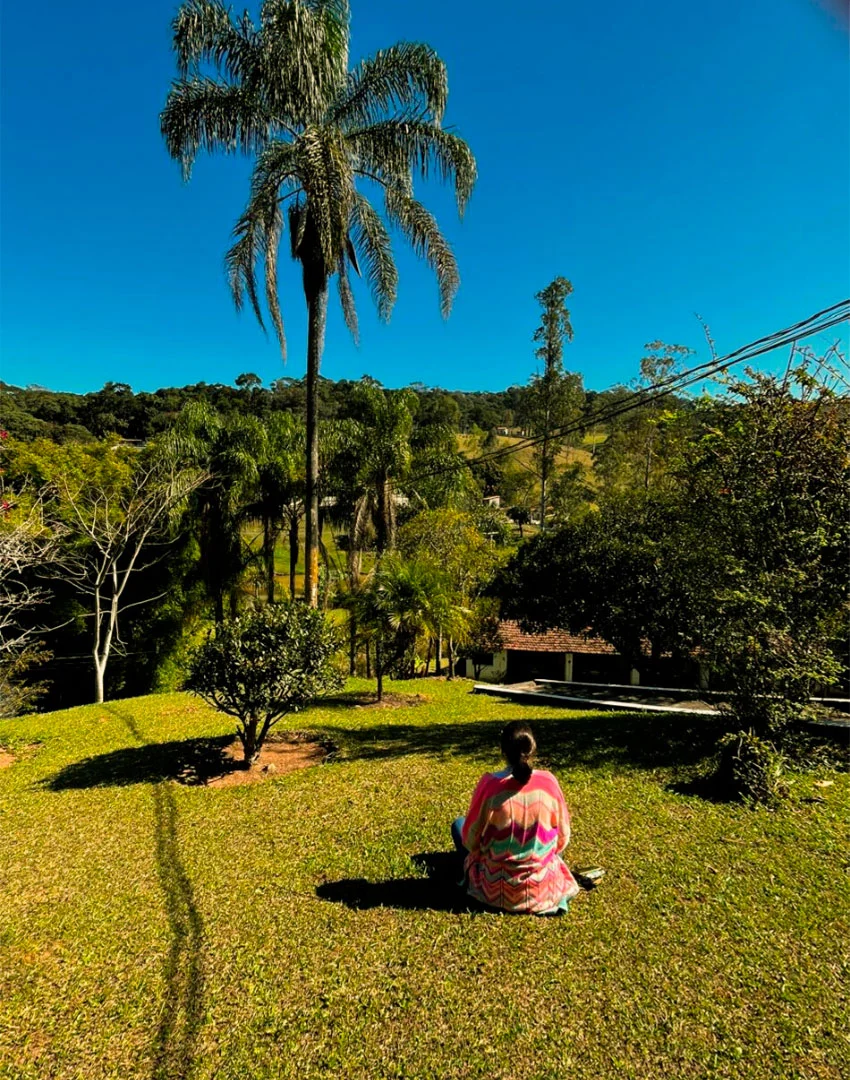 Pessoa sentada no jardim do Sítio Céu na Terra, cercada por árvores e gramado