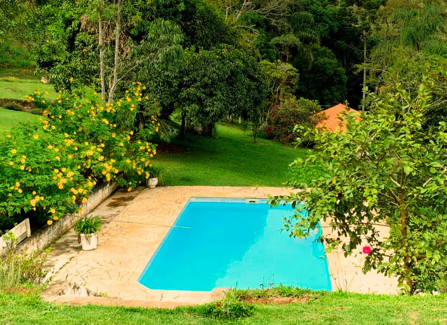 Piscina azul rodeada por vegetação e flores no Sítio Céu na Terra